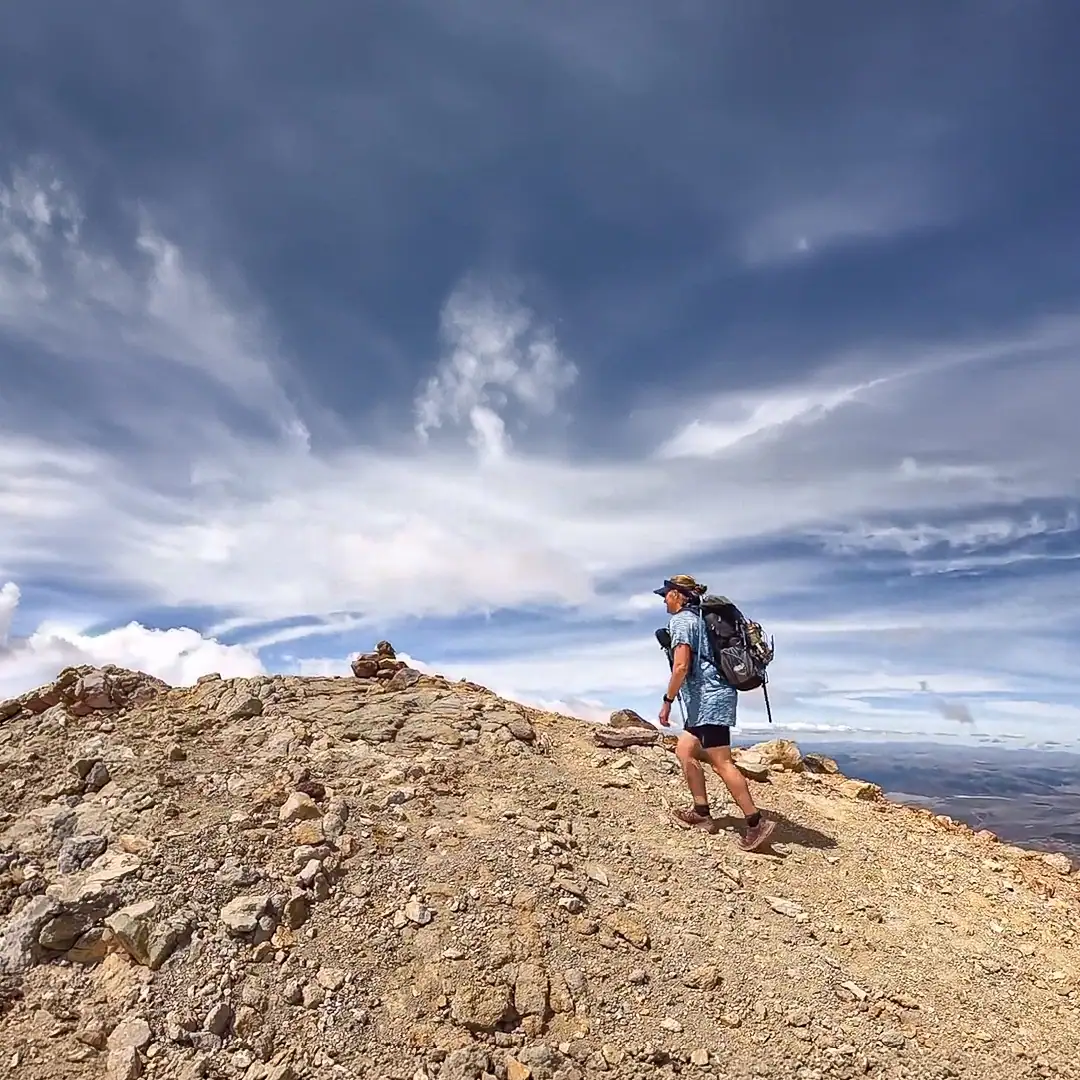Hiker summitting Tahurangi the highest peak of Mt Ruapehu in Tongariro National Park on a clear calm day