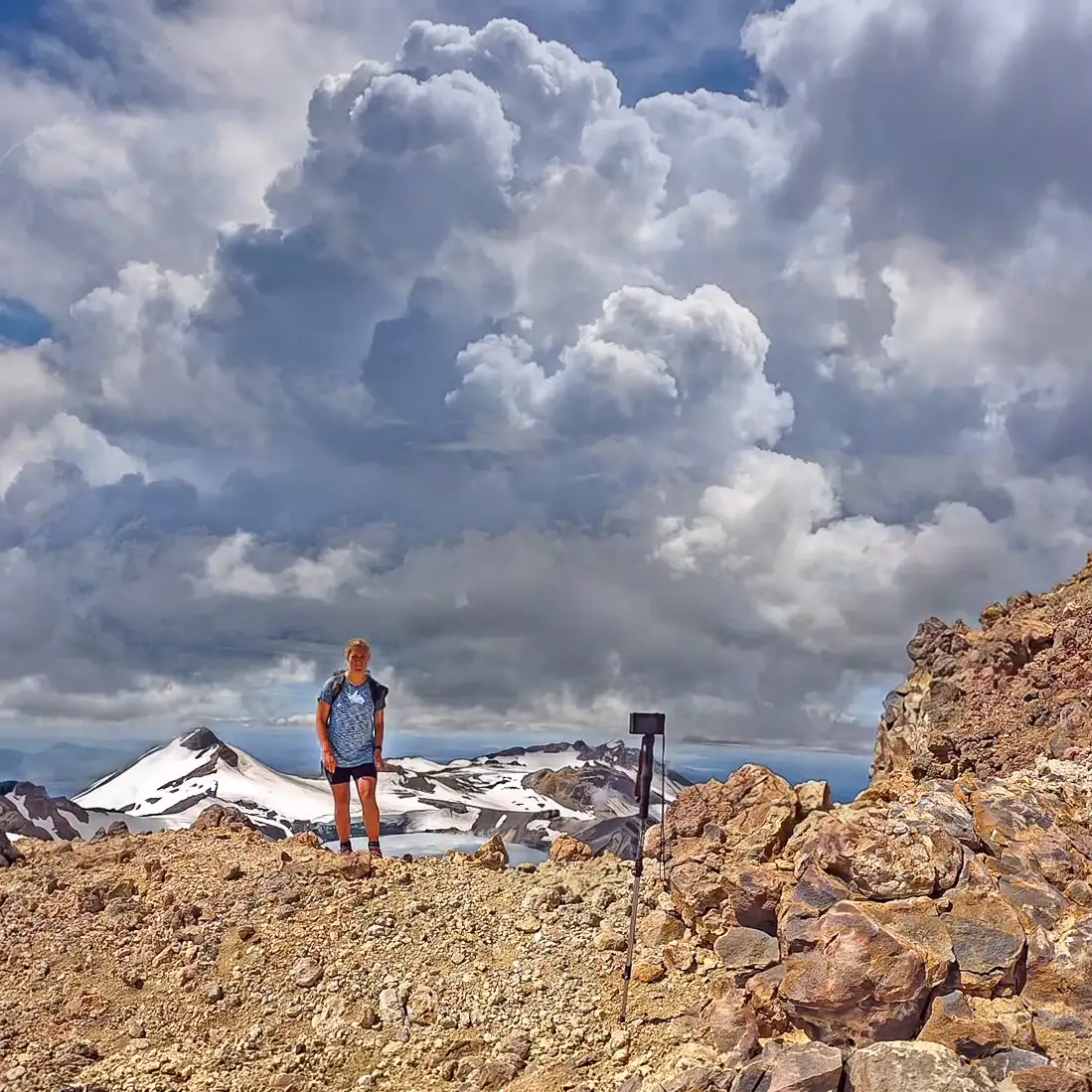 Hiker just below the summit of Tahurangi at Mt Ruapehu on a clear calm day but with dramatic cumulus clouds in the sky and with the Crater Lake and Summit Plateau in the background