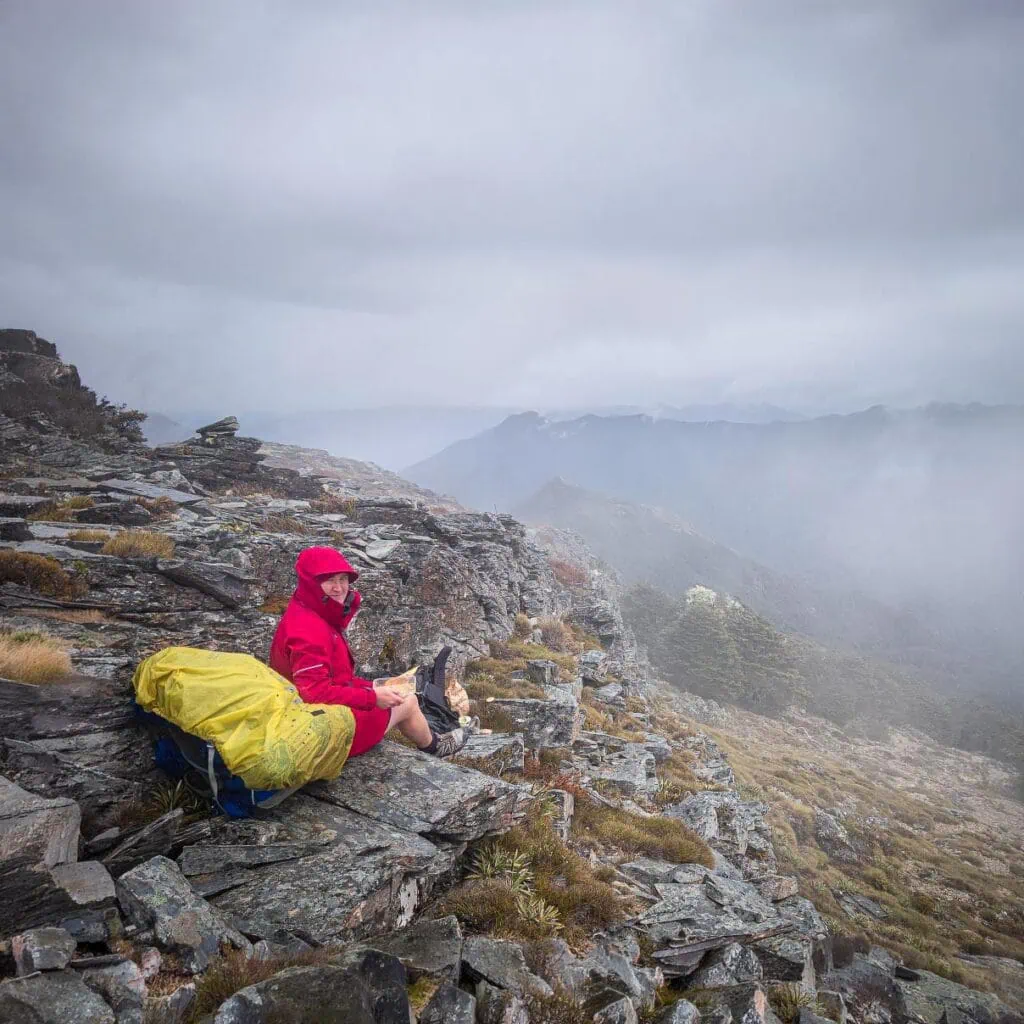 Sarah stops for a chilly lunch break with a nice view through the swirling mist above lake Chalice