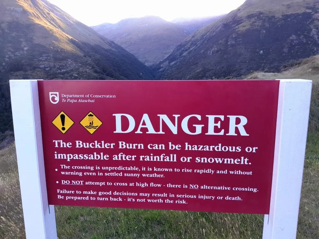 Department of Conservation (DOC) danger sign for the Buckler Burn crossing on the McIntosh Loop Track, warning hikers of rapid water rises and hazardous conditions after rain or snowmelt