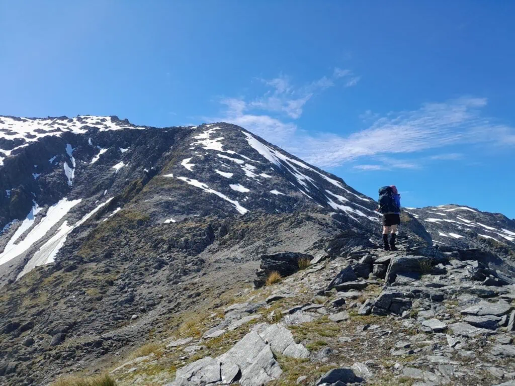 A hiker with a backpack looking toward the snowy ridgeline on the Mt. Adams route during a steep climb.
