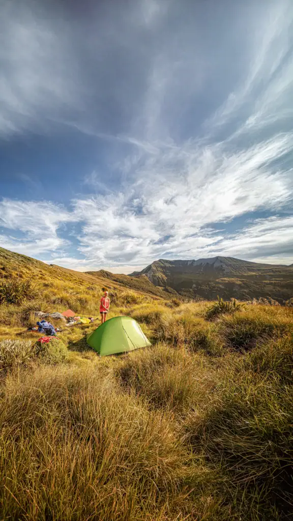 Sarah camping in the tussock on the Matiri Range on a fine evening with Haystack in the background