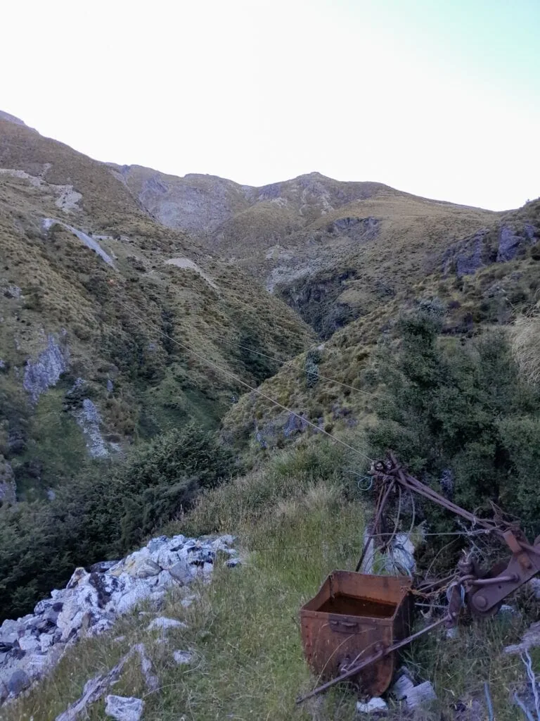 Historic aerial cableway and rusty ore bucket relics from the scheelite mining era, located along the Judah Track in the Whakaari Conservation Area near Glenorchy.