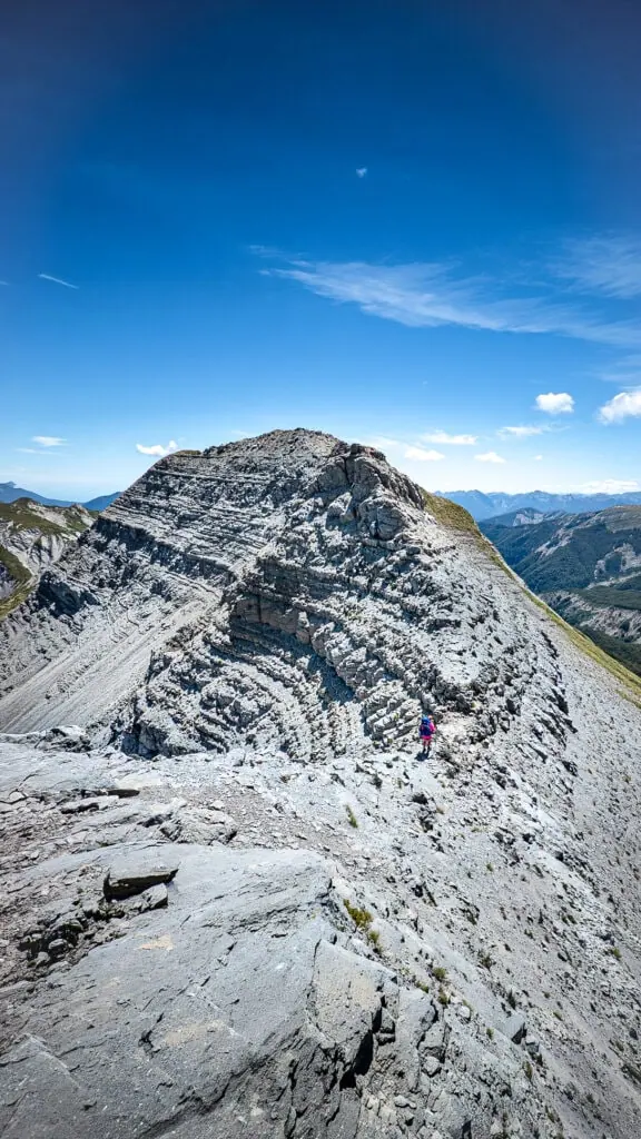 Hiker walking on a narrow ridge with Dramatic mudstone formations in an area known as the Haystack in the Matiri Range