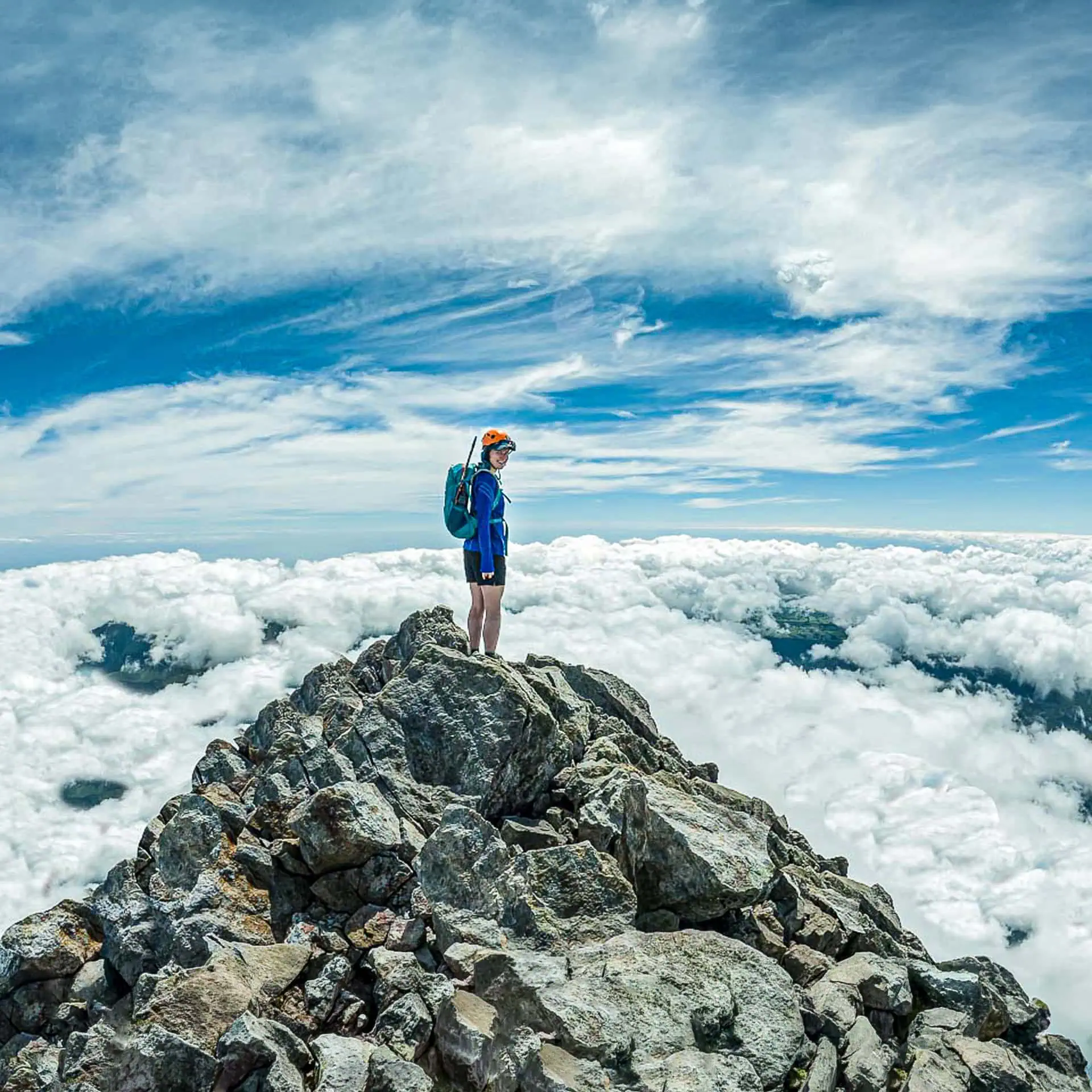 Hiker stands on the summit of the Sharks Tooth high above a sea of cloud  seemingly on top of the world.