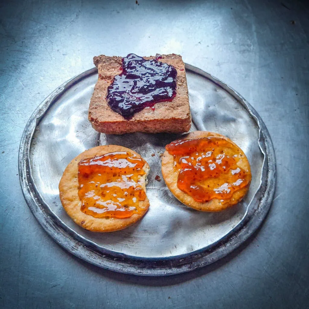 Jam on Tararua Biscuits and mealmates on a pot lid on a metal bench in Jam Hut, Seaward Kaikōura Range, Ka Whata Tu o Rakihouia Clarence