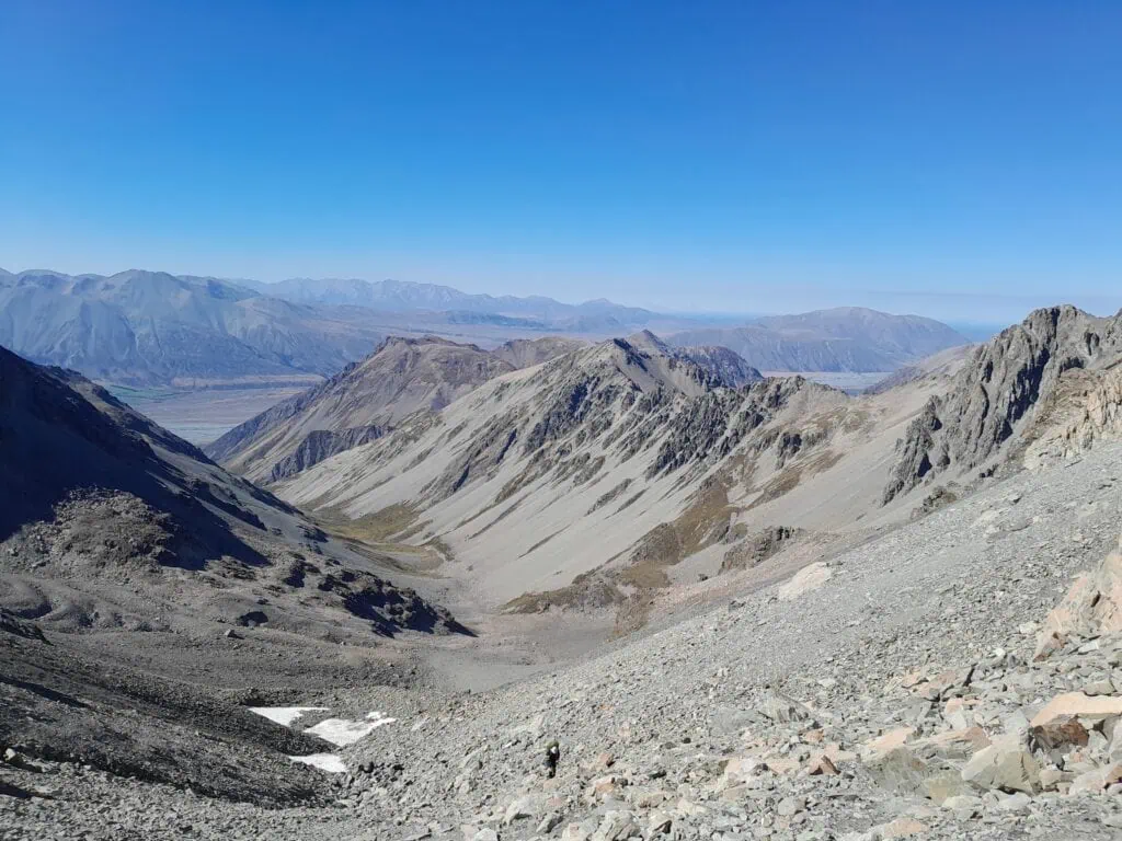 Looking back toward the Rangitata River valley from the steep scree ascent to Alma Col (2,139m) with patches of snow just below the col. The image shows the rugged peaks and glaciated valleys of the Two Thumb Range, Canterbury high country. Mt Potts is visible in the distance - the flat peak.