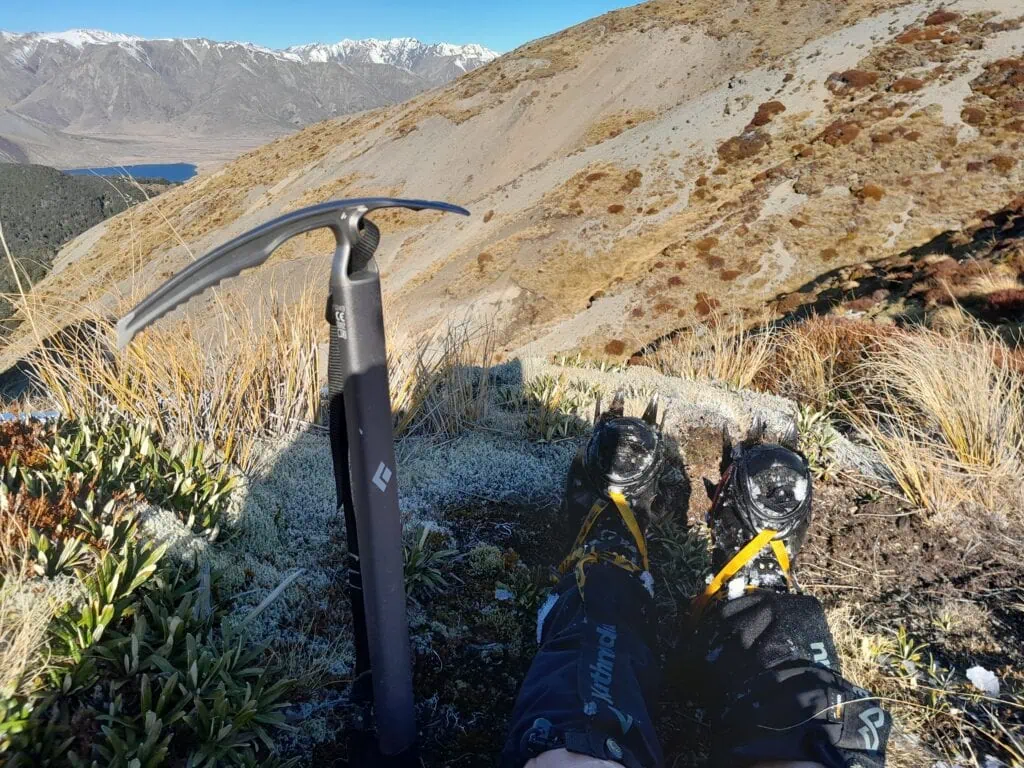 An ice axe and crampons amongst tussock on Mt Princess with Lake Tennyson and the Crimea Range in the background in St James Conservation Area