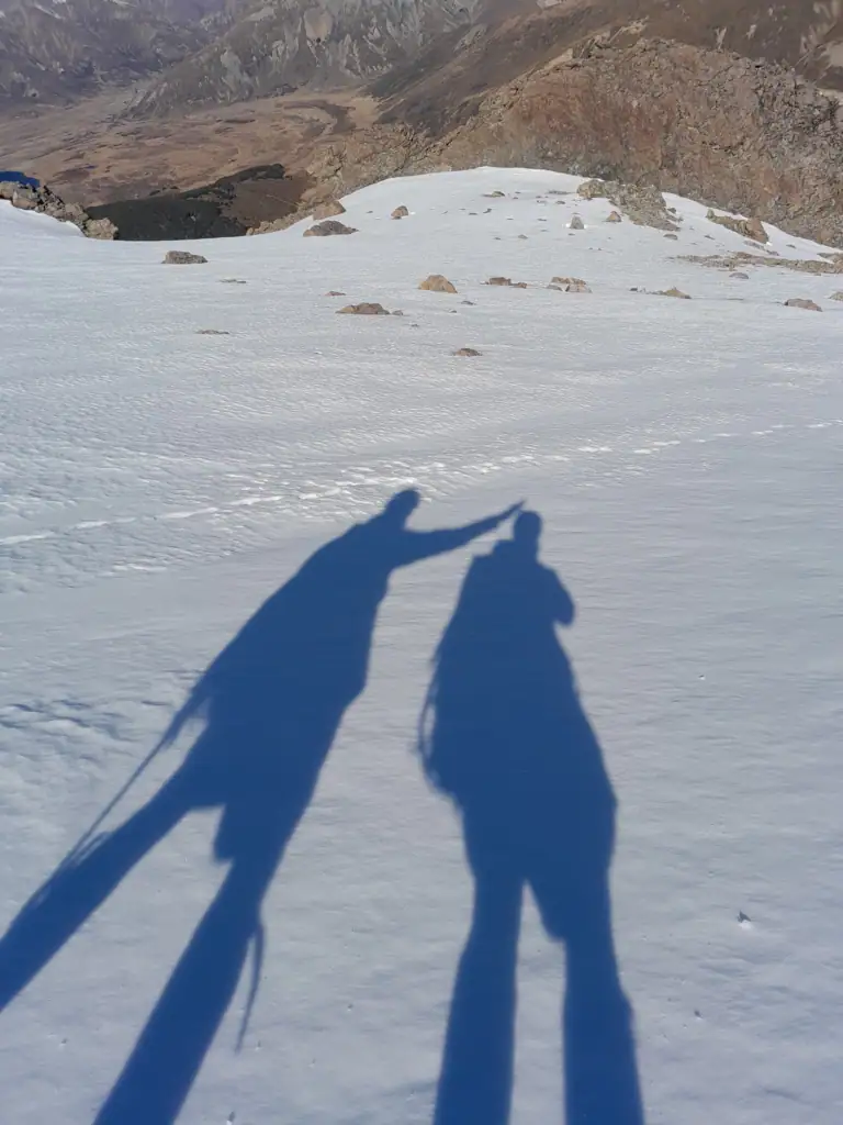 Elongated shadows of two hikers on a snowy slope on the descent from Princess Bath, St James Conservation Area