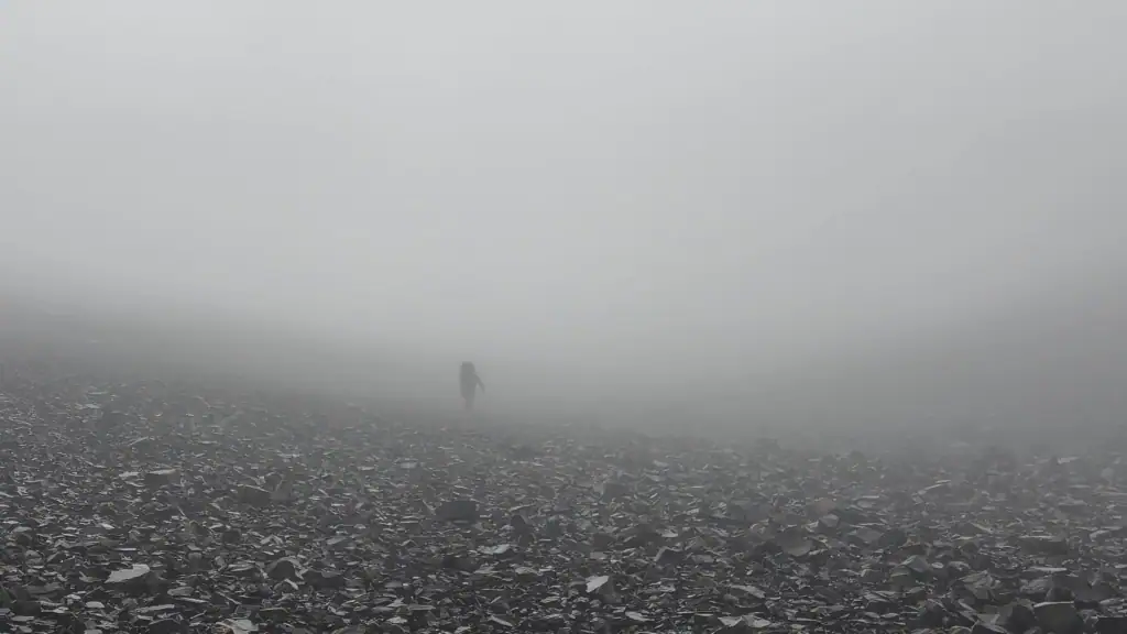 A sole tramper climbs through dense mist over rocks towards Brabazon Saddle in the Two Thumb Range