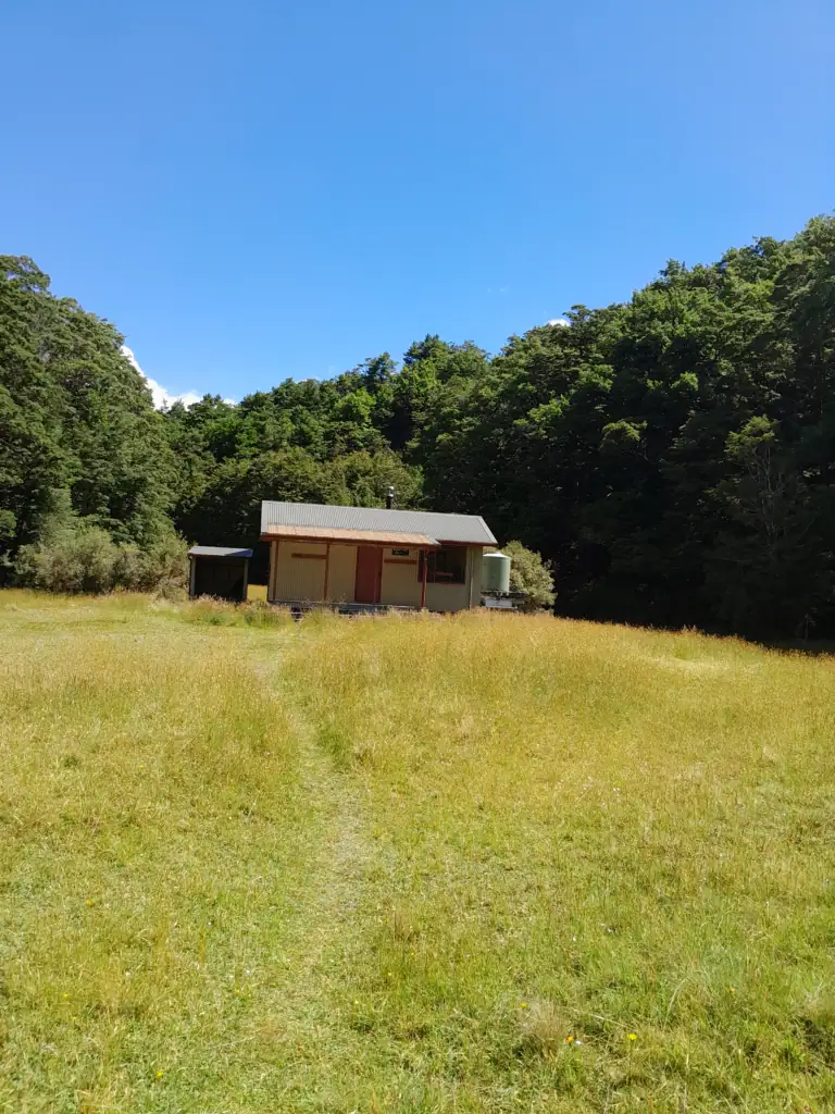 Morgan Hut standing amongst a grassy area surrounded by bush and a blue sky 
