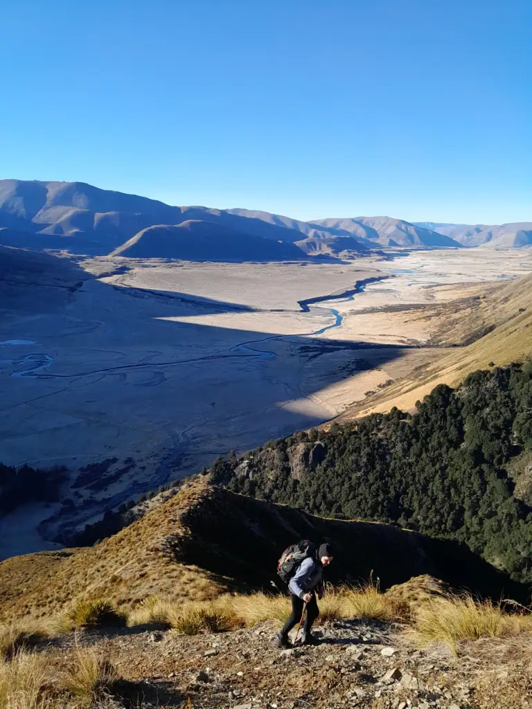 A hiker climbs above a frost covered Ahuriri Valley in New Zealand to the peak of Mt Gladwish, 1861m for views of the Southern Alps & Mt Aspiring. 
