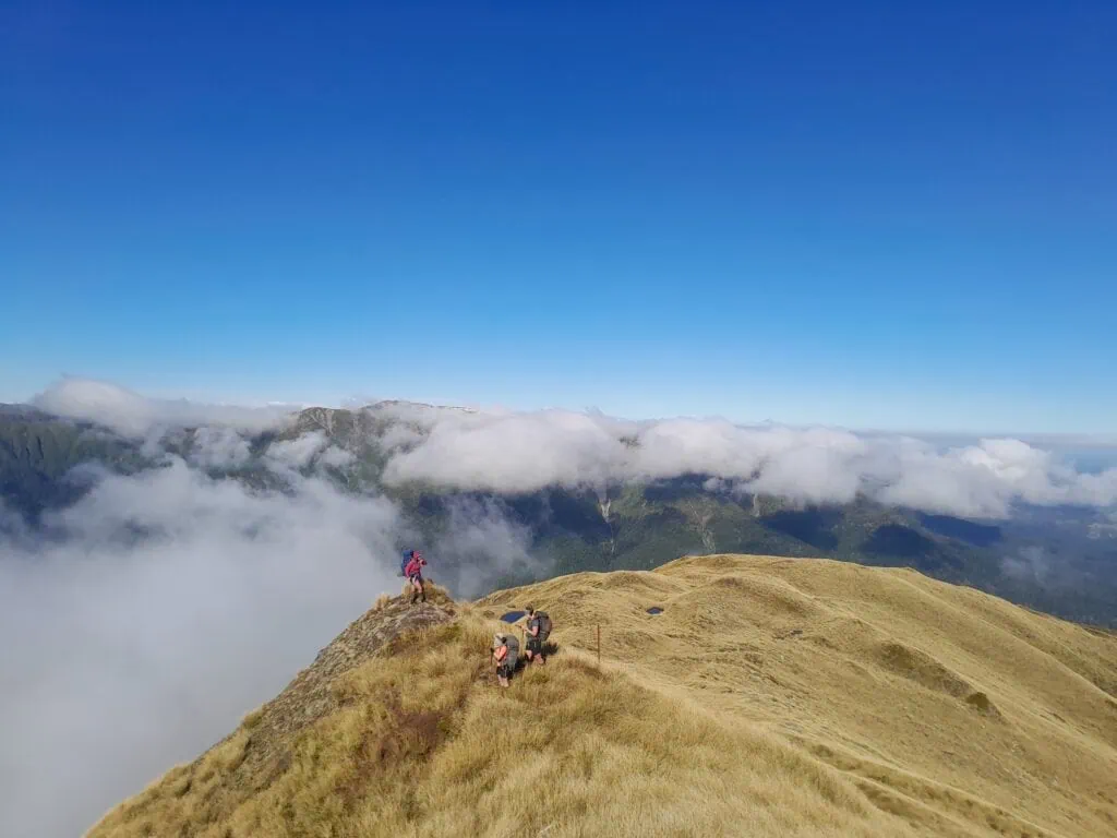 Three trampers amongst tussock and tarns above the clouds on the climb to Wooden Peg in the Ruahine Range