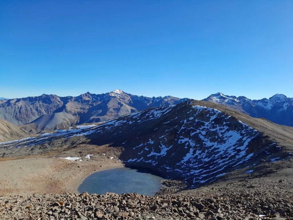 A frozen alpine tarn near Pinnacle on the way to Dumb-bell lake with the snow covered Barrier Range in the background