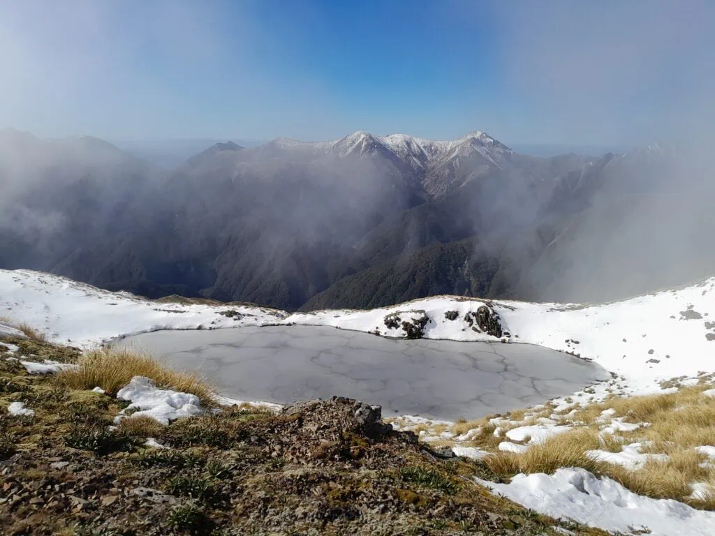 A frozen tarn under the peak Mangaweka with clouds rolling in looking across to Rongioteatua on the Ruahine Main Range
