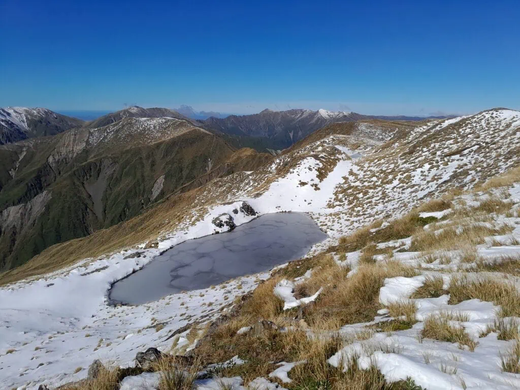 Snow covered tussock, peaks and a frozen tarn on the highest peak, Mangaweka, in the Ruahine Range.