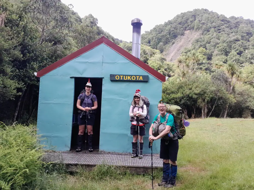 Three trampers stand outside a blue Otukota Hut in the Ruahine Range