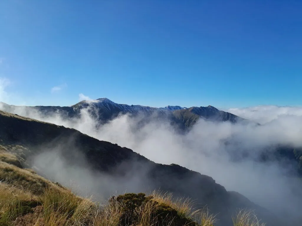 Clag rolling in over the Ruahine Main Range on a bluebird day while climbing towards Wooden Peg