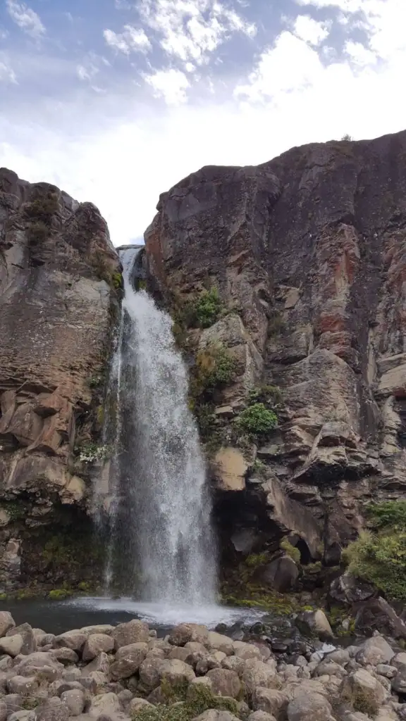 A 20-meter waterfall plunging over an ancient 15,000-year-old andesite lava flow into a boulder-fringed pool in Tongariro National Park