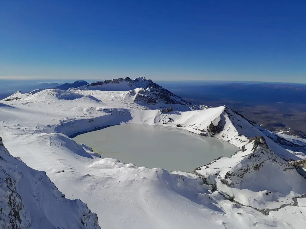 View of the snow surrounded Mt Ruapehu Crater Lake outlet from the summit of Te Ātaahua (Point 2757), Tongariro National Park. Te Heuheu, Tukino and Dome in the background