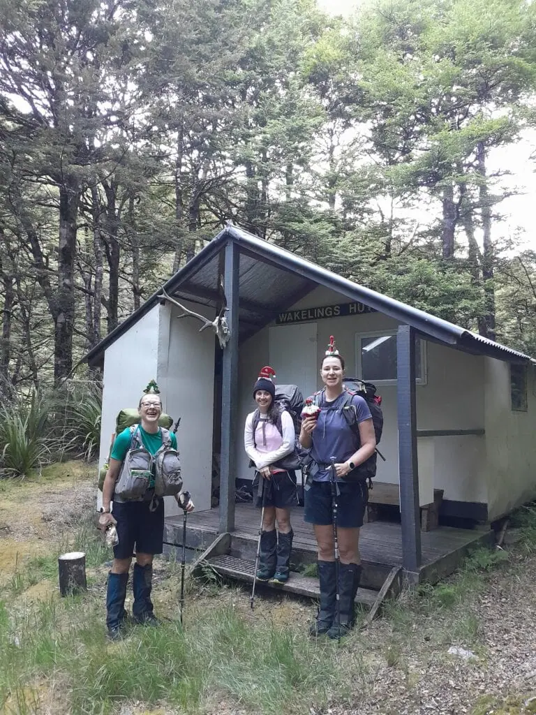 The exterior of the green corrugated iron Wakelings Hut, nestled in a grassy clearing surrounded by beech trees  in the Ruahine Forest Park.