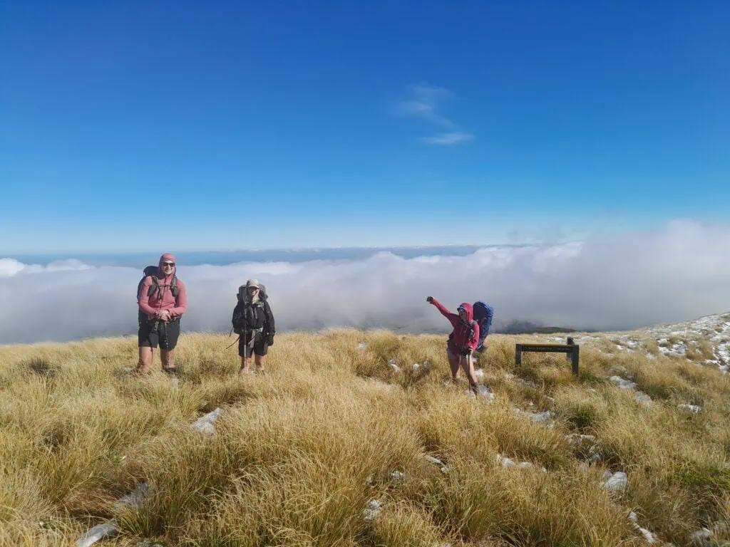 Three trampers at Wooden Peg with thick cloud behind them