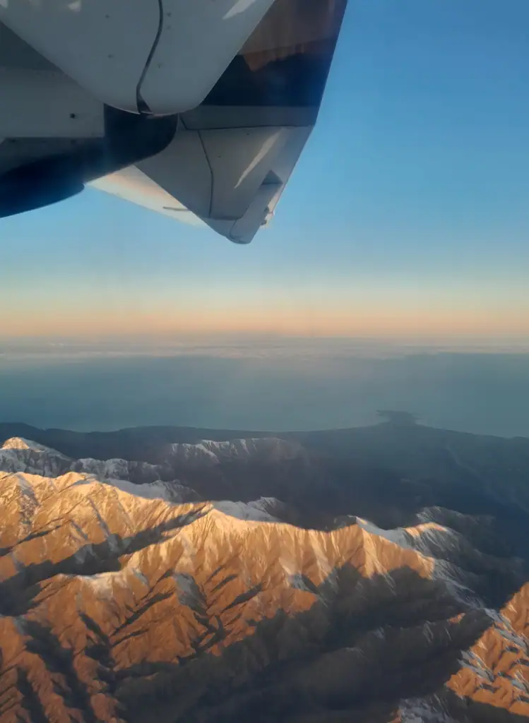 Aerial view of the snow-capped Kaikoura Range mountains in New Zealand at sunset, taken from an Air New Zealand airplane window