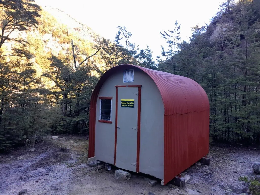 The historic, red corrugated iron Lower Salmon Creek Bivouac nestled in a clearing in the Mt Oxford forest, Canterbury