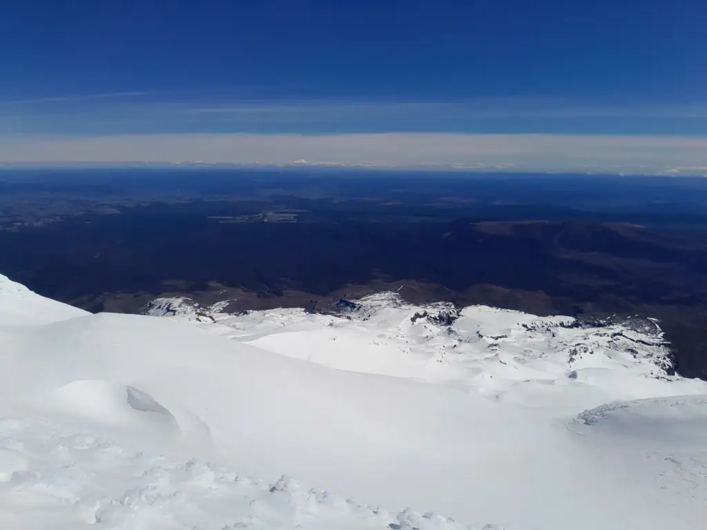 Expansive winter view looking west from Mt Ruapehu across the North Island landscape to the distant snow-capped volcanic cone of Mt Taranaki on the horizon.