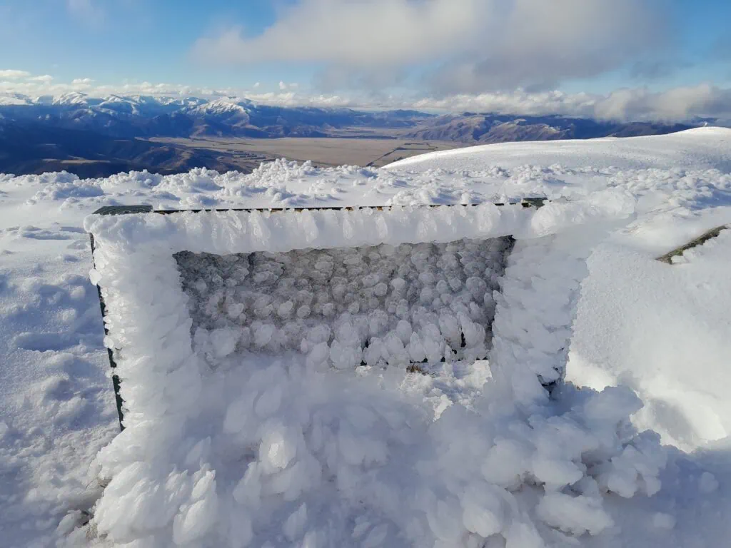 A Department of Conservation (DOC) track sign completely encased in heavy rime ice on the freezing summit of Mt Oxford.