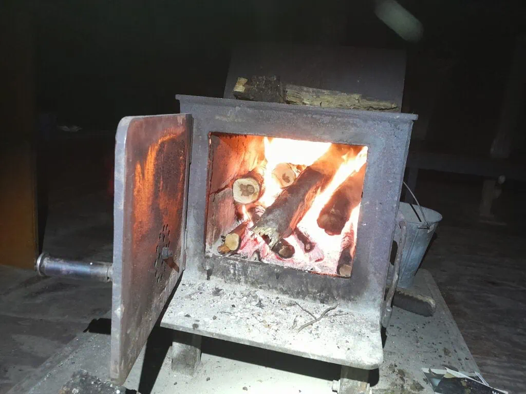 A bright, roaring log fire burning inside the cast iron woodburner stove to warm up Wharfedale Hut on a cold night, Mt Oxford Forest, Canterbury