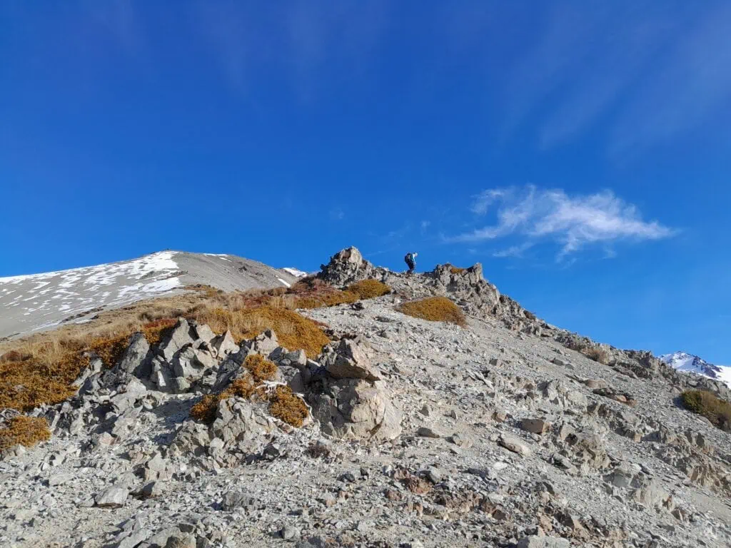A tramper scrambling up a steep, rocky section on the route on the unmarked approach to Mt Izard, Craigieburn Forest Park, Canterbury