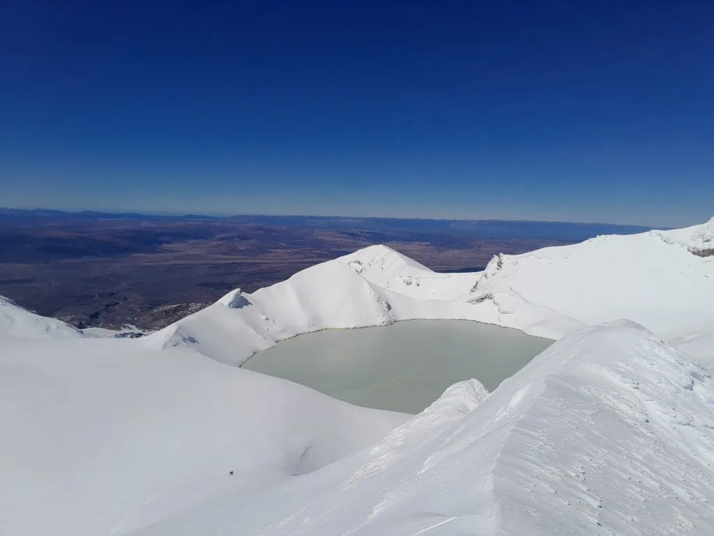 High-angle panoramic view of the volcanic Crater Lake on Mount Ruapehu, completely surrounded by steep, snow-covered walls and ridges in winter.