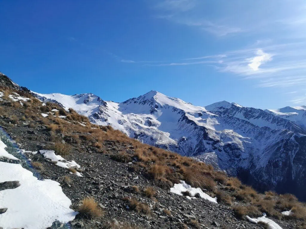 Tussock and rocky scree slopes in the foreground looking across to steep, snow-covered faces of Mt Cheeseman in Craigieburn Forest Park (Canterbury) while climbing up Mt Izard