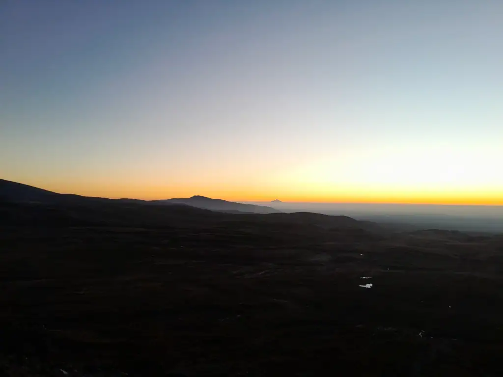 A tranquil alpine sunset over  Tongariro National Park, viewed from high above Upper Tama Lake in the deep evening light with Ngā Puna a Tama visible on the right, Mt Taranaki on the horizon in the centre and Hauhungatahi on the left. 