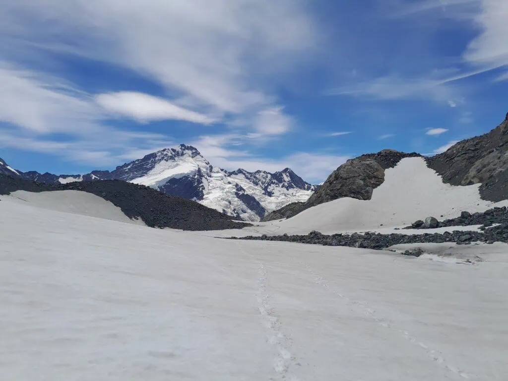 Footprints leading across the wide, snowy expanse of the Annette Plateau toward the snow-covered peak of Mt Sefton under a blue sky, Aoraki/Mt Cook National Park