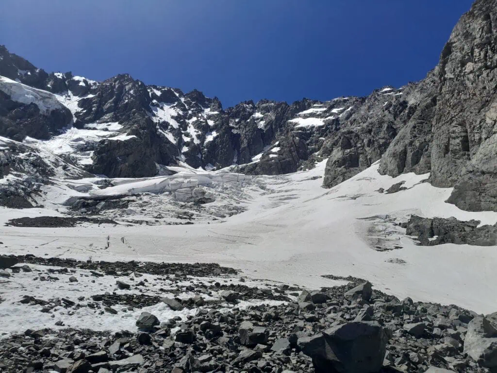 The upper snowfields of the Ashburton Glacier showcasing cracked ice formations and active crevasses beneath towering, dark rock ridges of the Arrowsmith Range, Hakatere Conservation Park, Canterbury