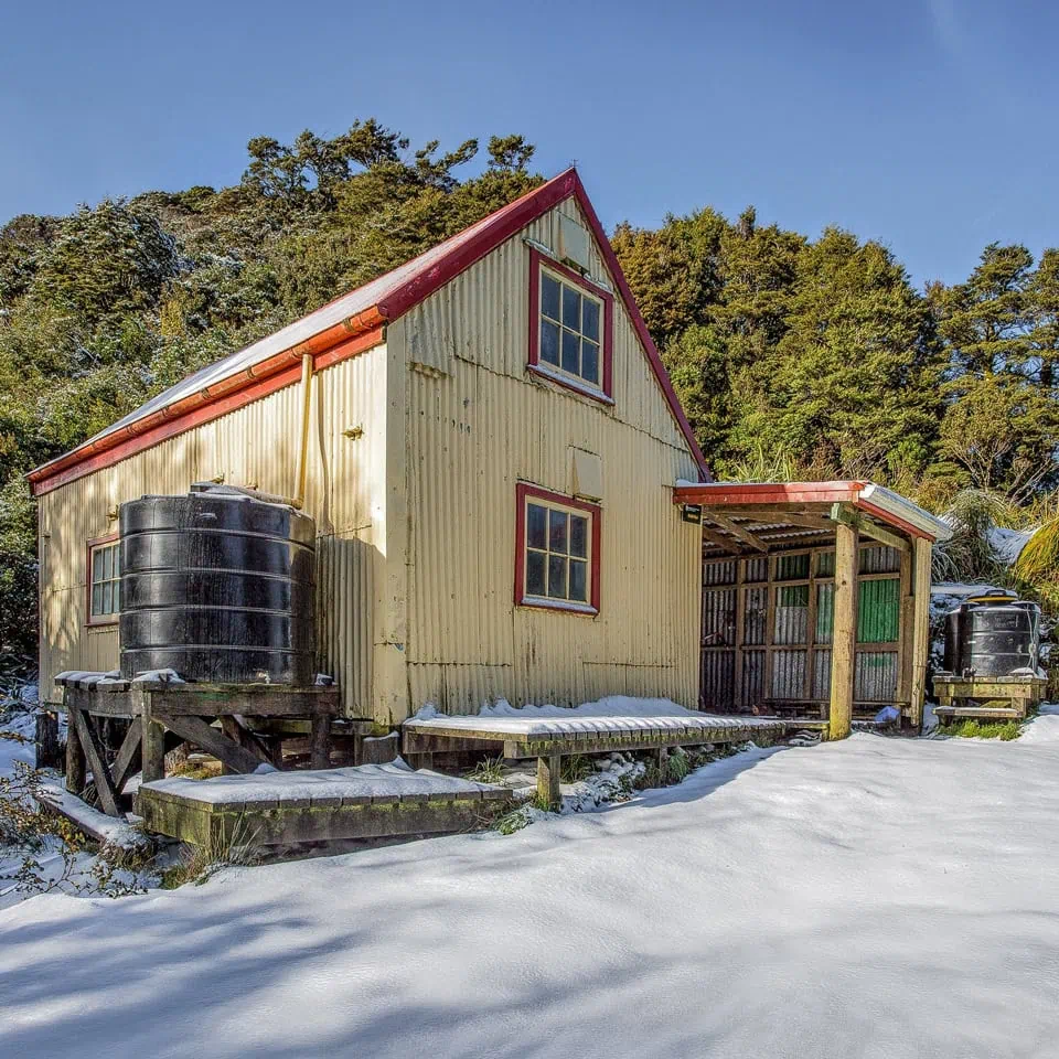 Field Hut in the Tararua Range on a clear day with blue sky but with unusual snow on the ground. Technically the oldest tramping hut in the Tararua Range
