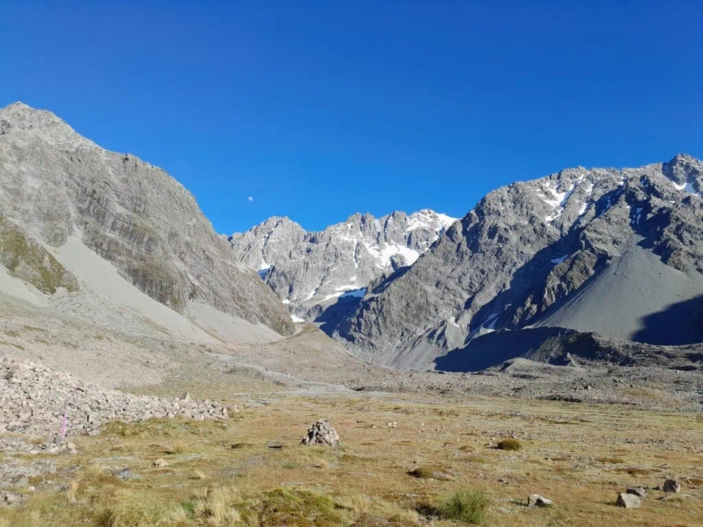 Looking across the wide, rocky alpine flats at the head of the Cameron Valley toward the steep rock walls and permanent snowfields of the Arrowsmith Range, Hakatere Conservation park, Canterbury