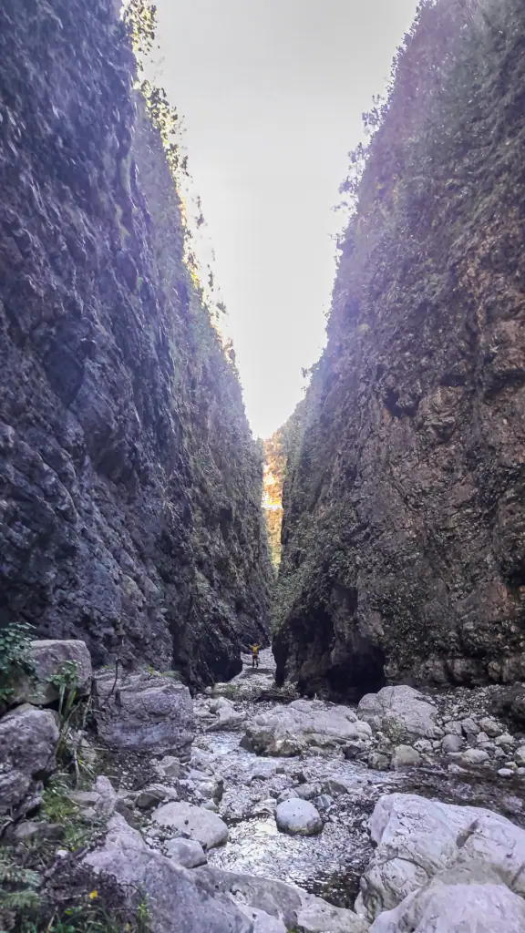 A tramper standing in the rocky stream bed of a towering, narrow limestone slot canyon in Brian Boru Gorge. Located in in Isolated Hill Reserve in the Seaward Kaikōura Range
