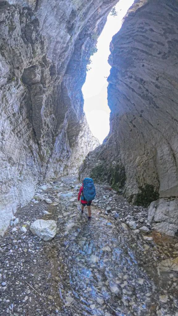 A tramper with a blue backpack walking upstream through the shallow water of a spectacular, winding limestone canyon in Sawcut Gorge, in Isolated Hill Reserve in the Seaward Kaikōura Range

