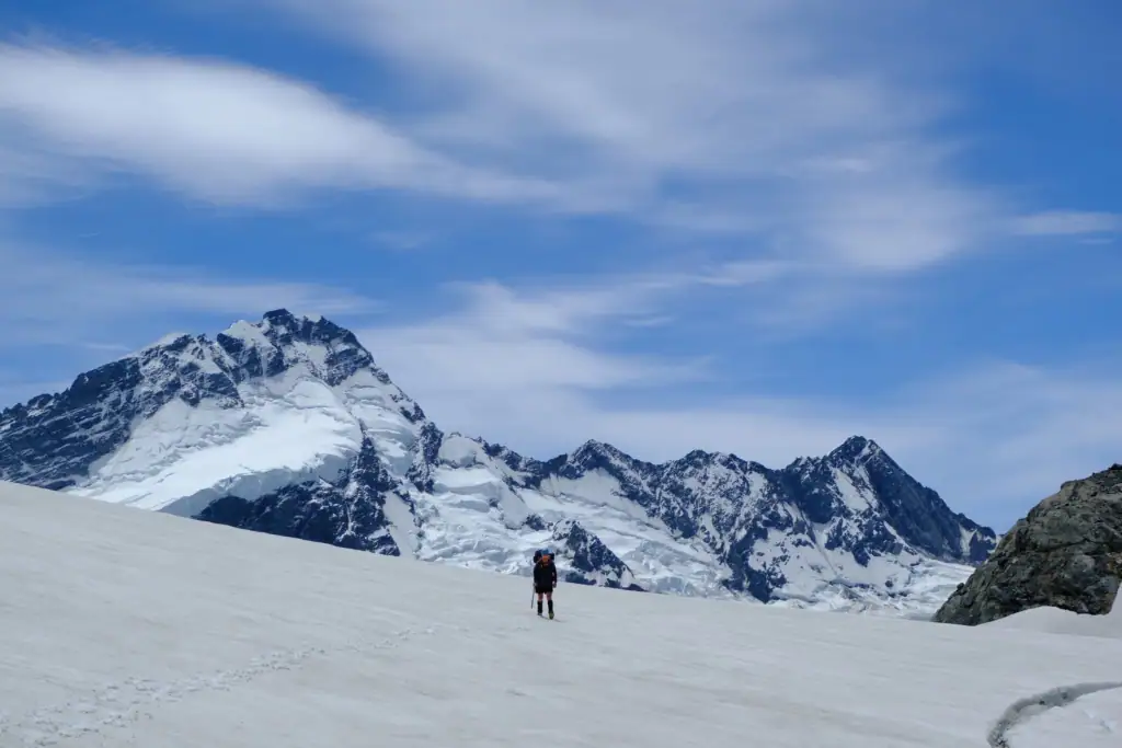 A hiker walking on the Annette Plateau with the steep, snow covered Mt Sefton behind her, Aoraki/Mt Cook National Park
