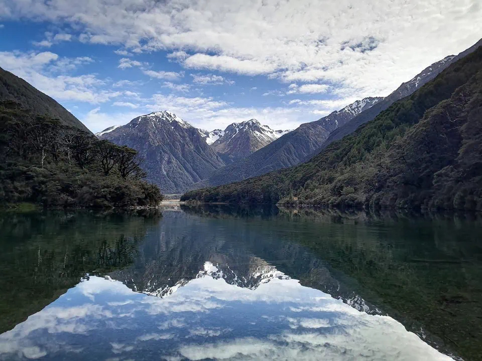 Perfectly still, glassy turquoise waters of Lake Minchin reflecting the blue sky, clouds, and snow-dusted peaks of Arthur's Pass National Park, above Poulter Valley, Canterbury
