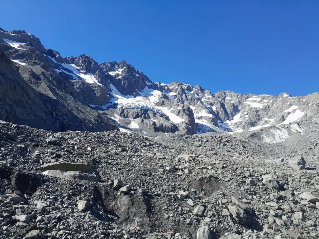 A massive, challenging moraine wall consisting of loose grey rocks and scree, which trampers must descend after traversing the Ashburton Glacier. Arrowsmith Range toering above. Located in Hakatere Conservation Park, Canterbury