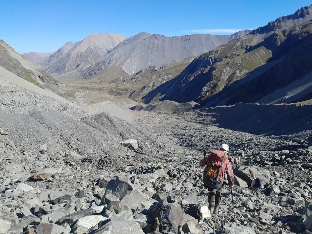 Trampers carefully route-finding down a steep, highly technical moraine wall of loose grey boulders and unstable rocks leading off the Ashburton Glacier, In the Arrowsmith Range, Hakatere Conservation Park, Canterbury