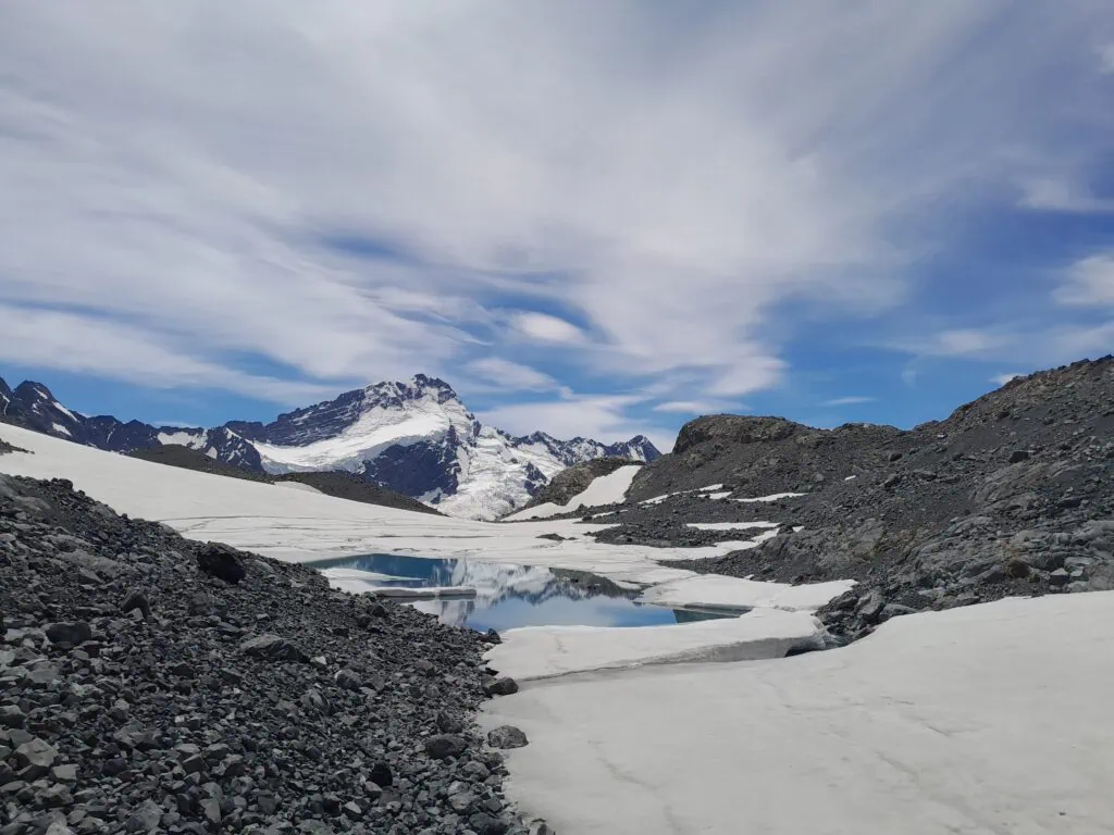The snow-covered peak of Mt Sefton reflecting clearly in a small, still emerald pool on the glacier ice sheets of the Annette Plateau, Aoraki/Mt Cook National Park.