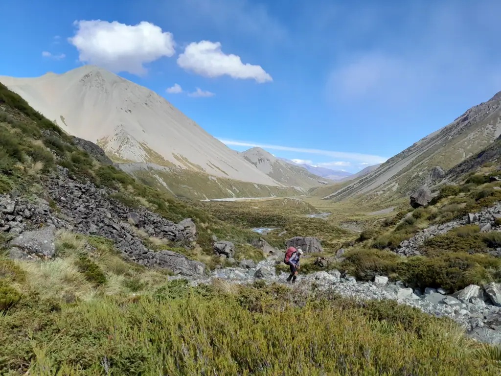 A single tramper with a large backpack navigates a rocky, boulder-filled track in the upper Cameron Valley on the route to Cameron Hut, Hakatere Conservation Park, Canterbury