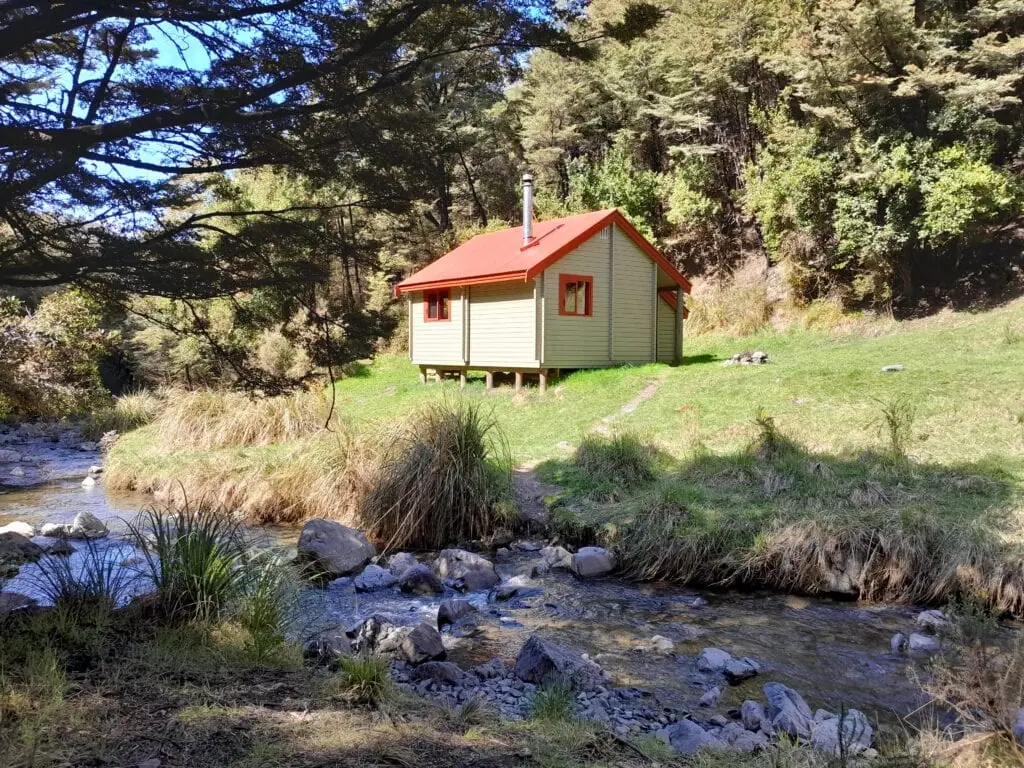 Exterior of the Standard 7-bunk Pinchgut Hut situated on a grassy flat next to the Okuku River stream in Mount Thomas Forest Conservation Area, Canterbury Foothills.