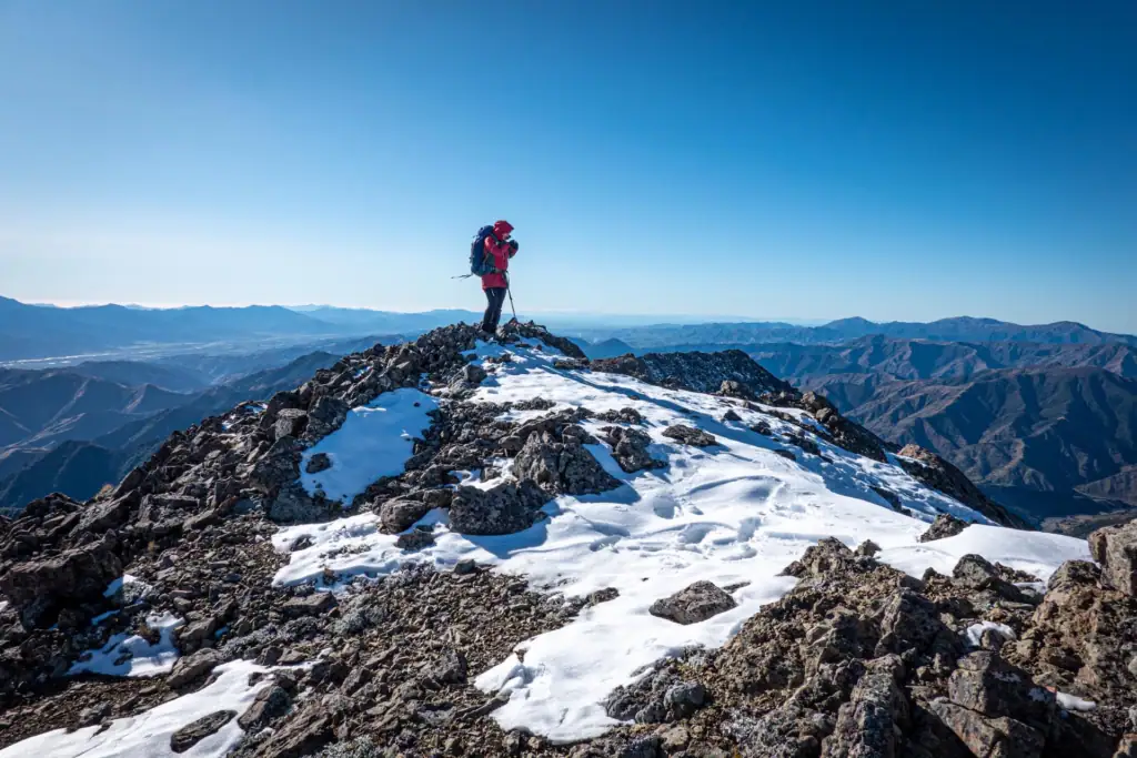 Tramper standing on snow-dusted rocky peak at Spot Height 1951m near Mt Bounds in Leatham Conservation Area