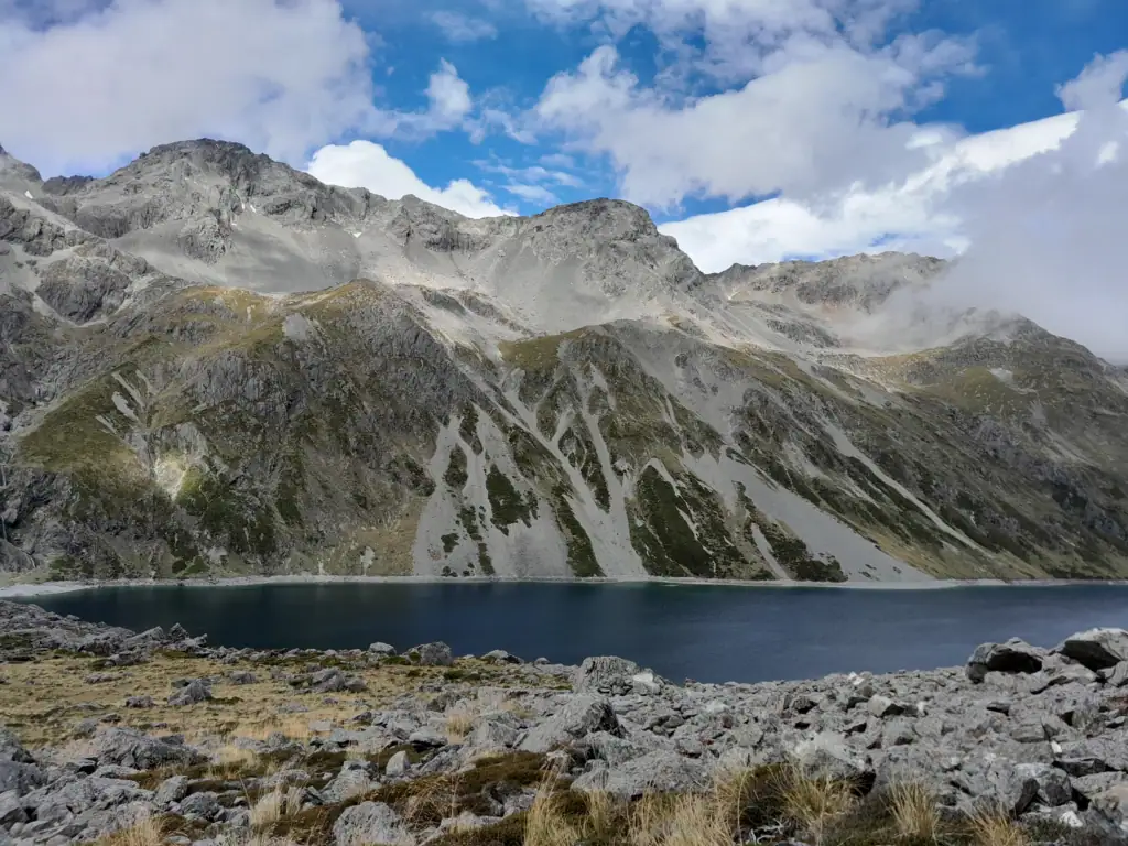 Shoreline view across Lake Constance looking at steep mountain ridges from the boulder-covered moraine wall on the Waiau Pass route, Nelson lakes National Park